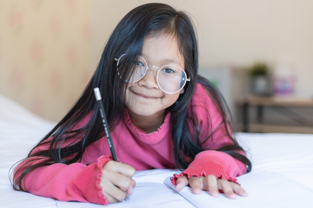 Cute asian girl thinking writing notes on the bed