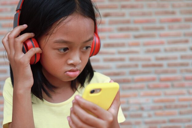 A cute Asian girl uses a red wireless headphone to listen to music on her phone