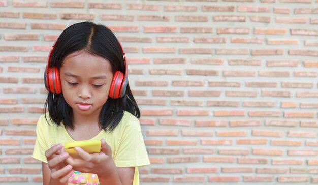 A cute Asian girl uses a red wireless headphone to listen to music on her phone