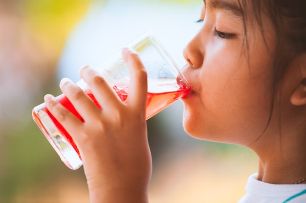 Cute asian little child girl drinking red juice water with ice from glass