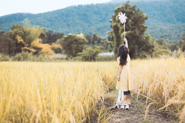 Cute asian little child girl playing with wind turbine in the paddy field in vintage color tone