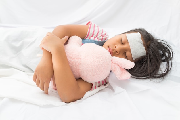 Cute asian little girl with fever reducer stick forehead and sleeping hug rabbit doll in t