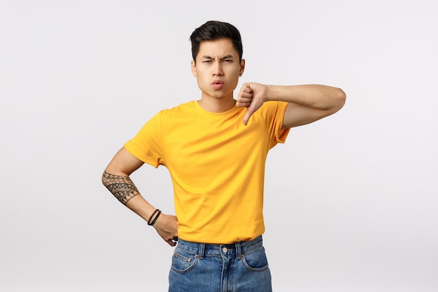 Cute asian man in yellow t-shirt giving thumb down