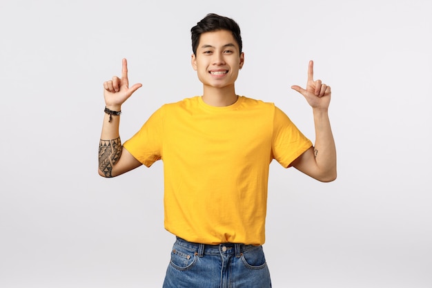 Cute asian man in yellow t-shirt pointing up