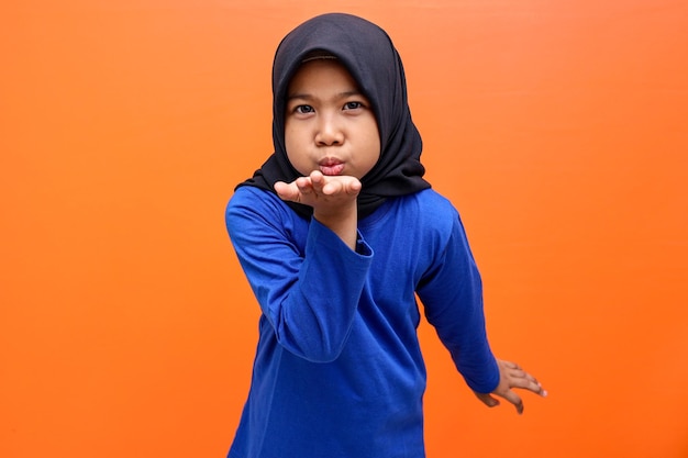 Cute Asian muslim girl blowing a kiss over orange background