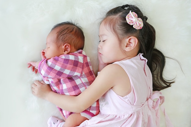 Cute Asian sister embracing sleeping newborn baby lying 