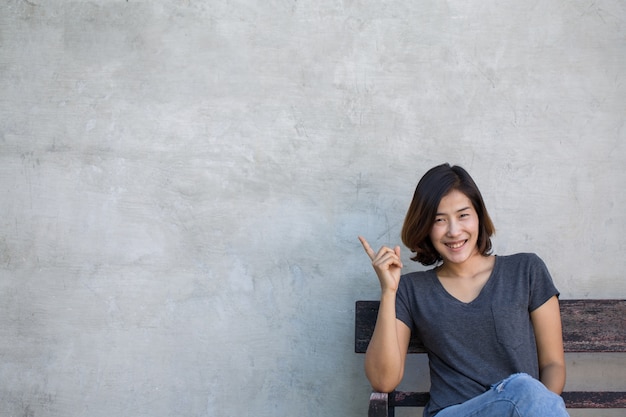 The cute Asian woman show something to you on the gray background.