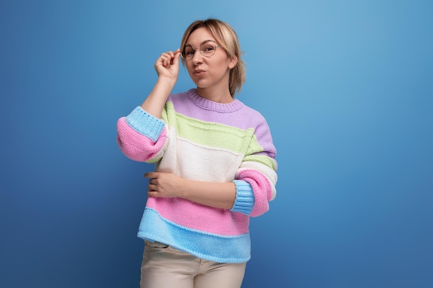 Cute attractive blond woman in a striped sweater posing thoughtfully on a blue background