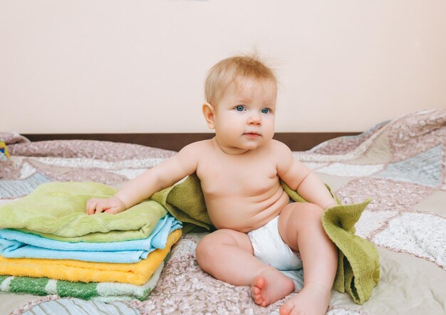 Cute baby 6 months old sitting next to a stack of towels