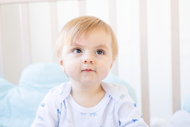 Cute baby boy blonde with big eyes closeup or portrait in the crib at home the concept of baby products and accessories