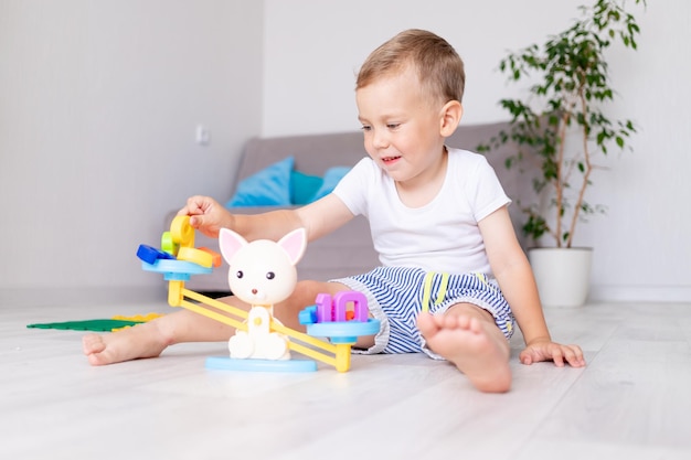 cute baby boy is playing with the scales at home on the floor trying to balance them and laughing