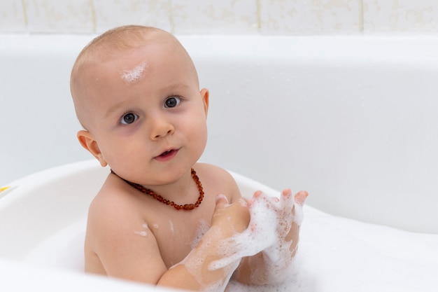 A cute baby boy is washing in the bathtub.