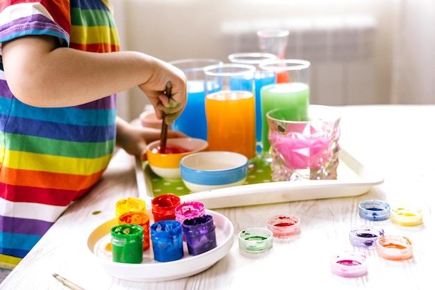 Cute baby boy learning mixing different colors with water and paint in containers early development