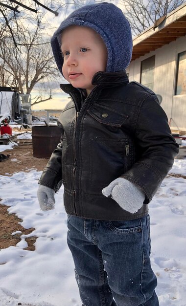 Photo cute baby boy looking away while standing on snow covered land