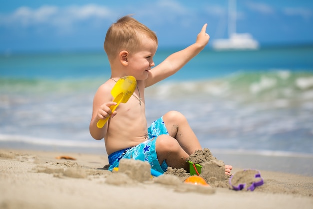 Cute baby boy playing with beach toys on tropical beach