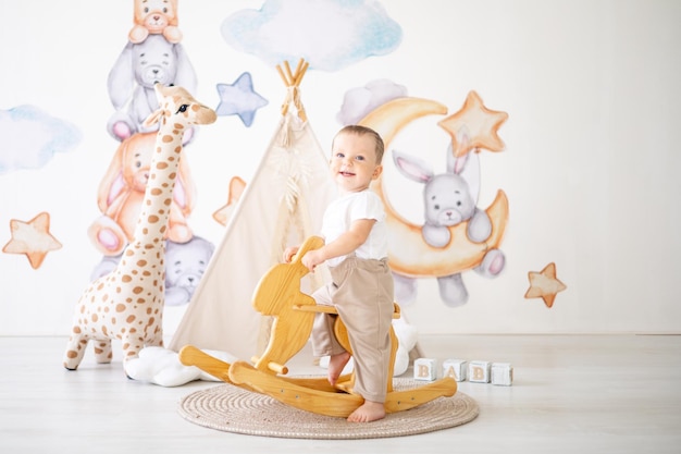 Cute baby boy rides a wooden rocking hare in the children's room at home educational toys for children