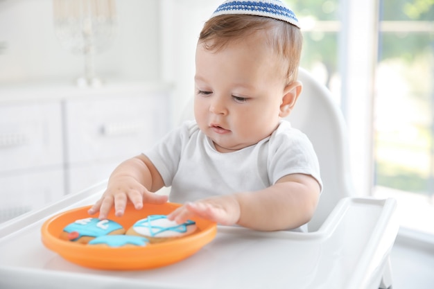 Cute baby eating festive cookies while sitting on high chair