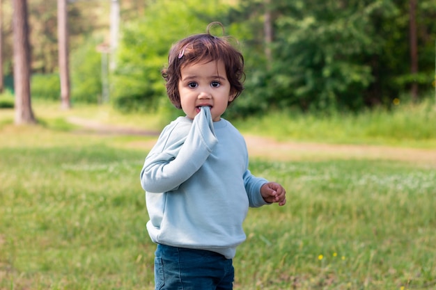 a cute baby girl holds a sweater sleeve in her mouth walking in nature