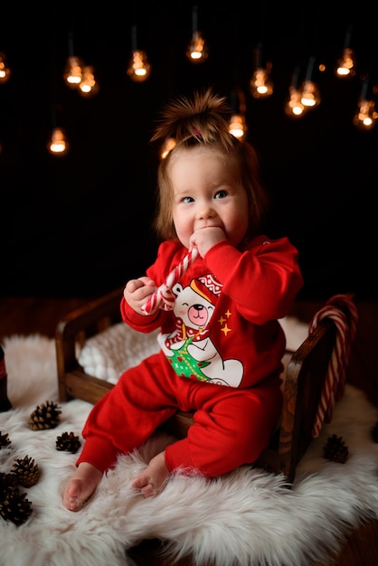 Cute baby girl in a red Christmas costume with retro garlands sits on a fur