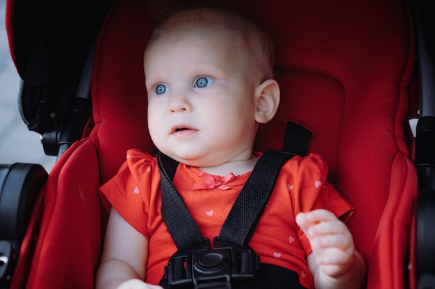 Cute baby girl sitting in red stroller