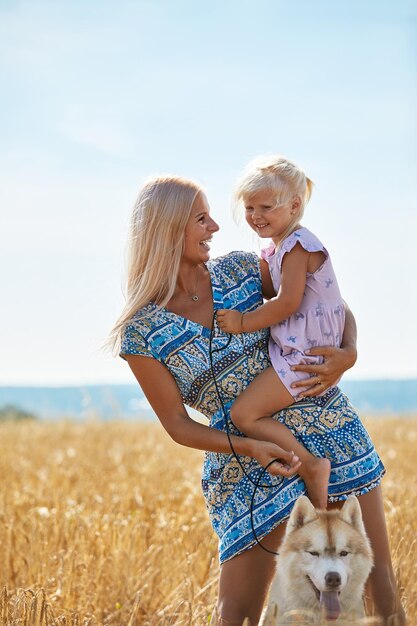 Cute baby girl with mom and dog on wheat field happy young family enjoy time together at the nature