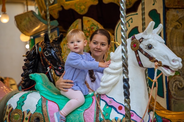 Cute baby girl with mother on the horse of old retro carousel prague czech republic