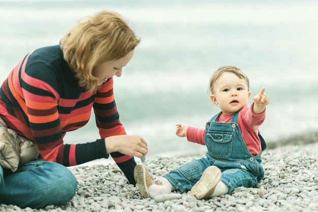 Cute baby and his mother playing with pebbles on the beach