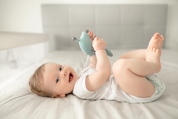 Cute baby infant boy wearing diaper playing with his feet in bed in a sunny bedroom