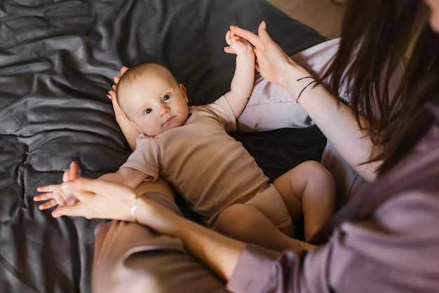 Cute baby is lying on the legs of a mother who is sitting on the bed