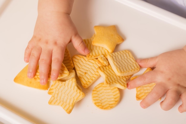 A cute baby is sitting in a child39s chair eating cookies Yellow background Baby food space for text