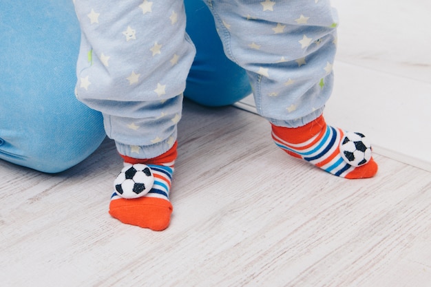 Cute baby learning to walk and make his first steps. mom is holding his hand. child's feet close up, copy space, socks with balls