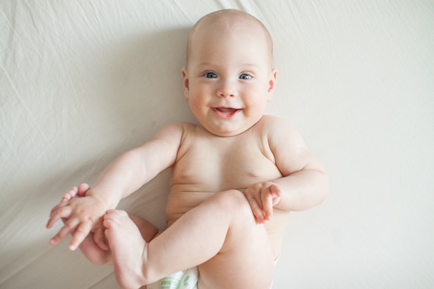 Cute baby lies on a white sheet and plays fun