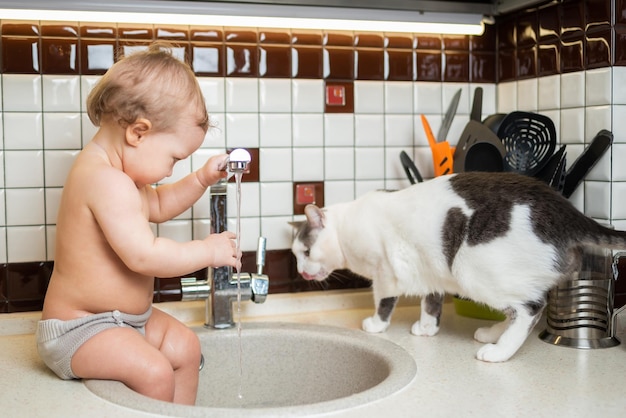 Cute baby playing in the kitchen sink with a cat