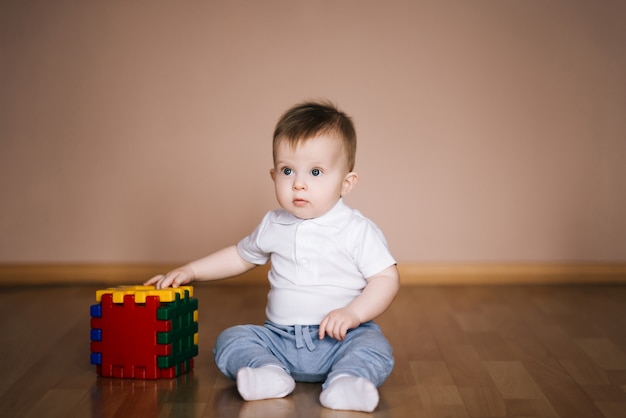 Cute baby sitting on the floor of the house playing with a multi-colored cube