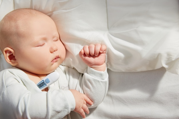 Cute baby sleeping on a pillow with a thermometer. Measure the temperature.