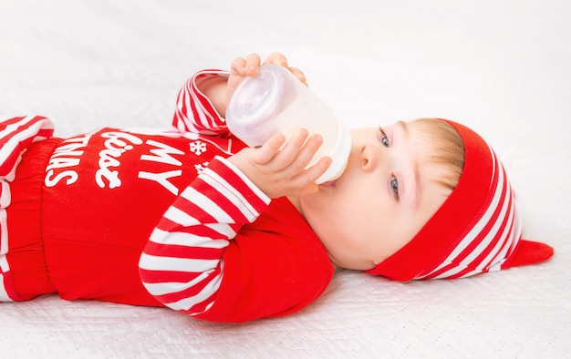 Cute baby wearing christmas suit eating milk from bottle lifestyle and winter holidays concept