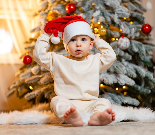 Cute baby wearing Santa hat Cute little boy near Christmas tree Christmas celebration