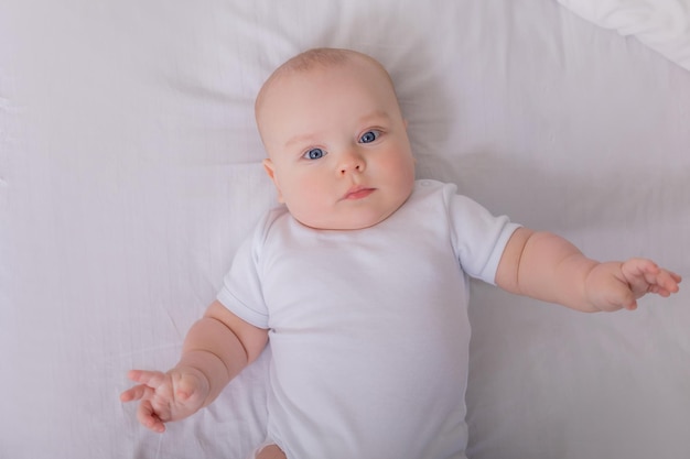 Cute baby in a white bodysuit lying in bed with cotton underwear top view space for text