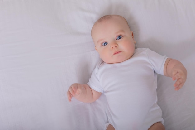 Cute baby in a white bodysuit lying in bed with cotton underwear top view space for text