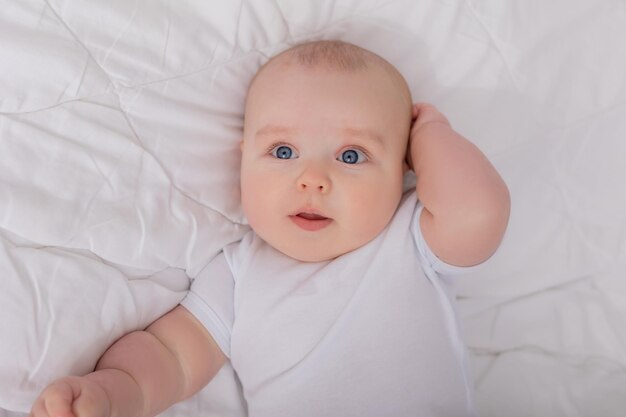 Cute baby in a white bodysuit lying in bed with cotton underwear top view space for text