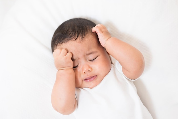 A cute baby in a white dress is crying. Stay with parents in the house