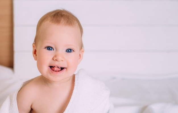 Cute baby with blue eyes wrapped in a white towel. Clean baby after bath, taking care of children.