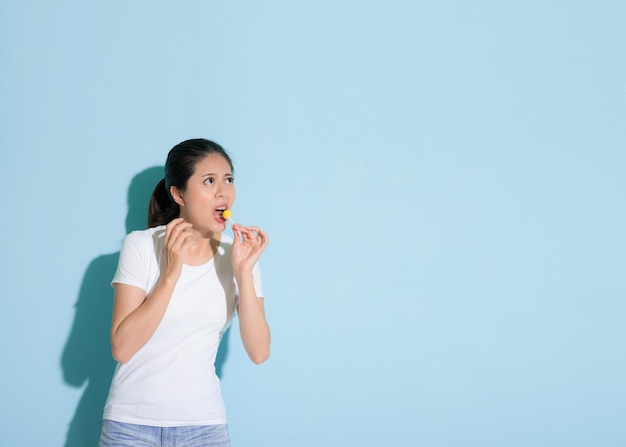 cute beautiful female model eating lollipop and looking empty area worry about tooth decay problem performance in blue wall background.