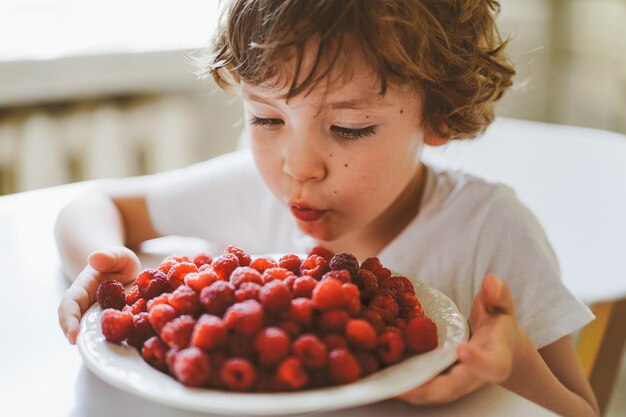 Cute beautiful little boy eating fresh raspberries. Healthy food, childhood and development.