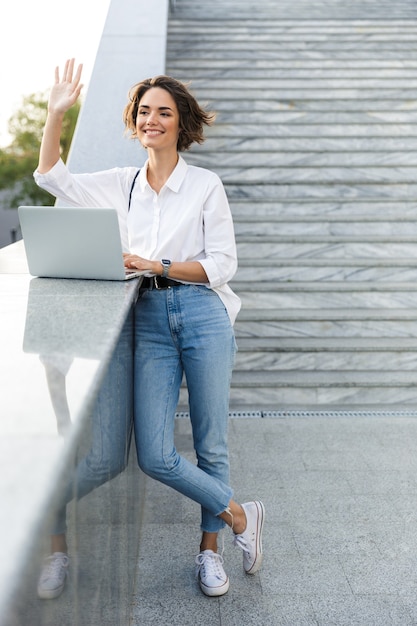 Cute beautiful woman walking outdoors using laptop computer