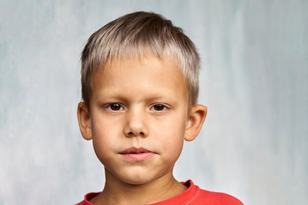 Cute blond boy frowns looking at camera on white background