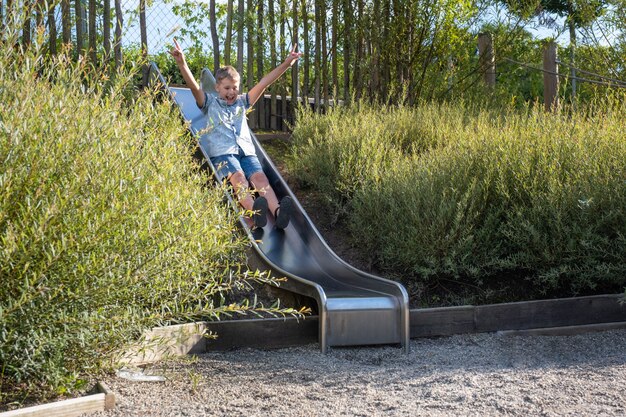 Cute blond boy swinging on a public playground swing. Kid play outdoors on warm sunny summer day.