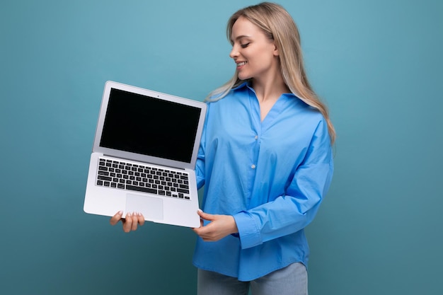 Cute blond girl showing laptop with blank space screen on blue background