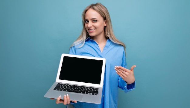 Cute blond girl with a laptop in her hands with a mocup on a blue background