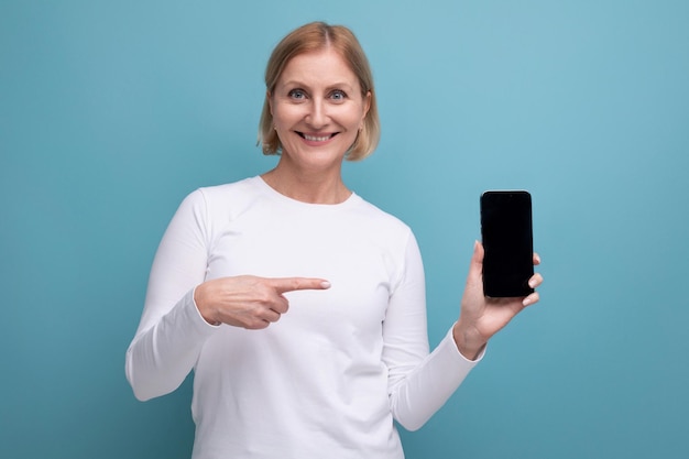 Cute blond middle aged woman demonstrating smartphone screen with mockup